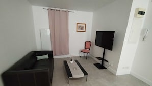 A living room with a dark brown sofa, a white coffee table, a pink curtain, a framed picture on the wall, and a flat-screen TV. - "Le Nid Dauphinois" fully equipped - Ideal for business, couples & families! (L'Albenc)