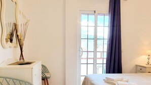 A hotel room with a bed, a chair, a desk, a window with curtains, and a view of the outside.