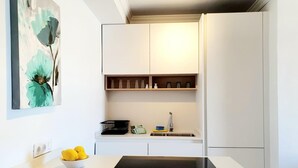 A modern kitchen with white cabinetry, a black countertop, and a painting of flowers on the wall.