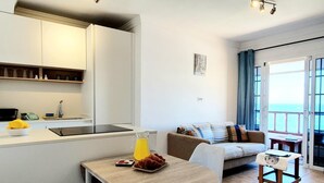 A modern kitchen with a dining area, a sofa, and a view of the sea.