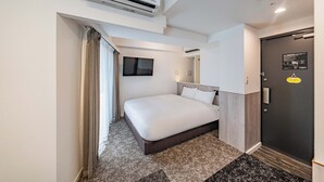 A modern hotel room with a large bed, an air conditioning unit, a shower area, and a door with a security badge.