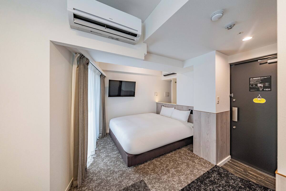 Una habitación de hotel moderna con una cama grande, un equipo de aire acondicionado, una zona de ducha y una puerta con tarjeta de seguridad.