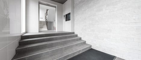 A staircase with a black mat at the bottom, leading to a door with a handrail.