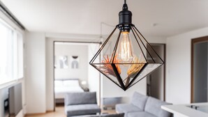 A modern living room with a geometric pendant light, a grey sofa, and a flat-screen TV. - GRANDIA 201 (Sapporo)
