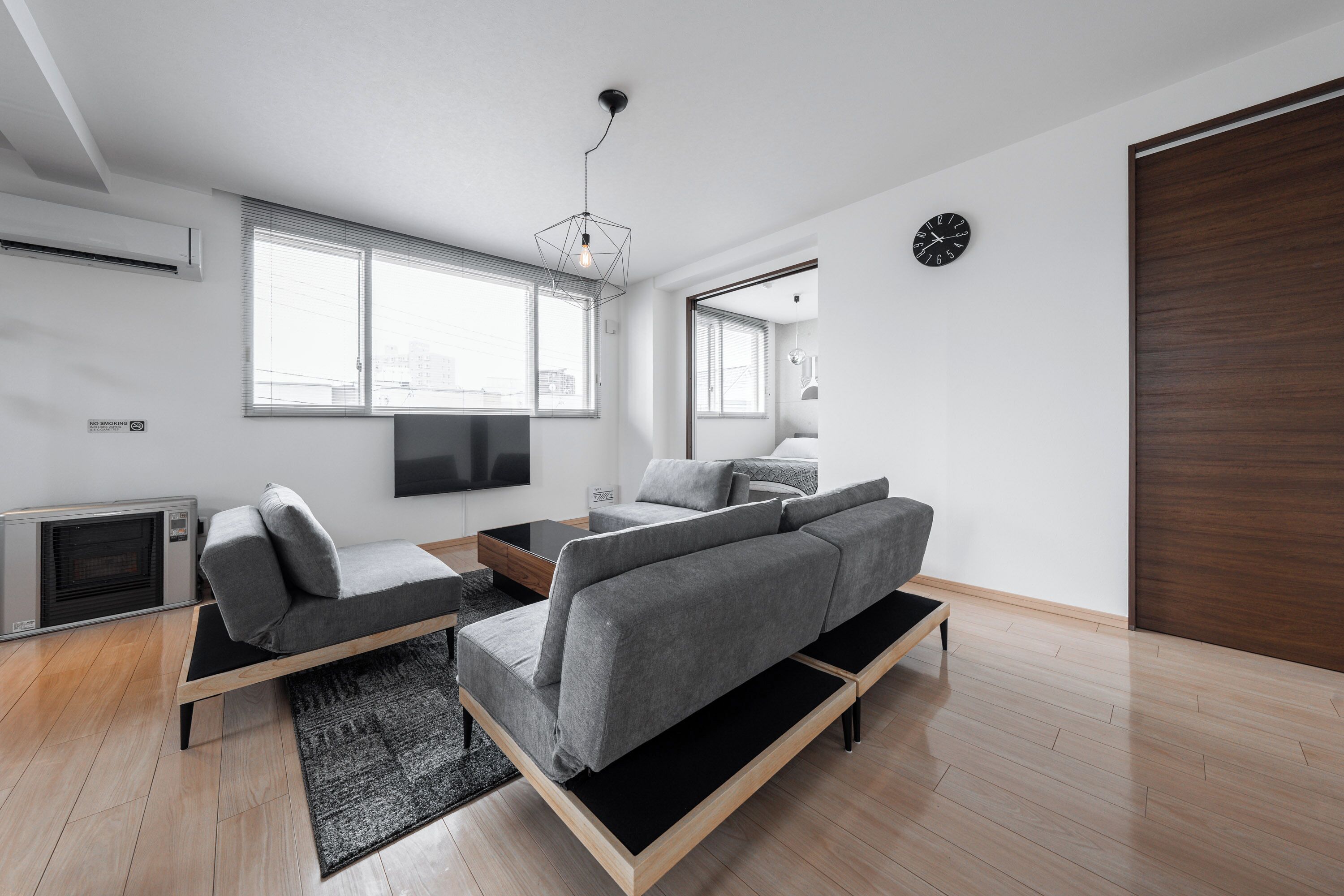 Un salon moderne avec un canapé, une table basse et un téléviseur à écran plat. Le sol est en bois et une grande fenêtre laisse entrer la lumière naturelle.
