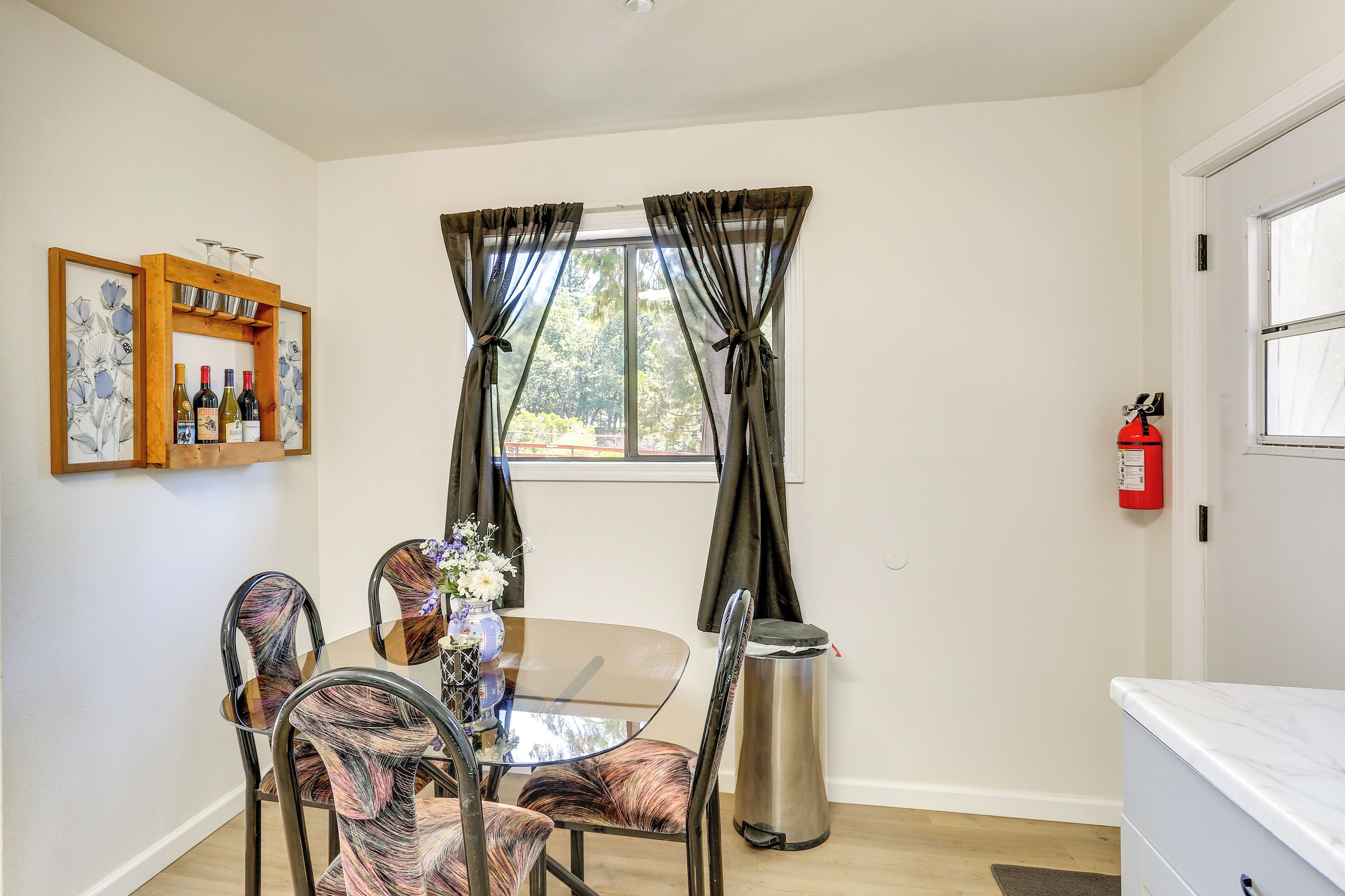 A dining area with a round table, chairs, a vase of flowers, a wine rack, and a fire extinguisher.