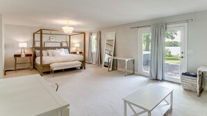 Um quarto amplo com uma cama grande, mesas de cabeceira, escrivaninha e porta de vidro corrediça para o exterior.
