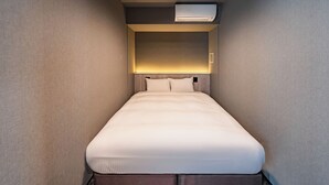 A hotel room with a bed, a headboard with built-in lighting, and an air conditioning unit.