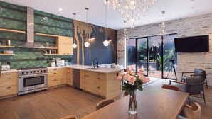 Una cocina moderna con armarios de madera, estufa de acero inoxidable y una zona de comedor con mesa y sillas de madera.