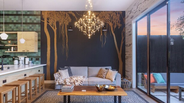 Un espacio habitable moderno con cocina, un sofá grande, una mesa de centro y vistas amplias a través de grandes ventanales.