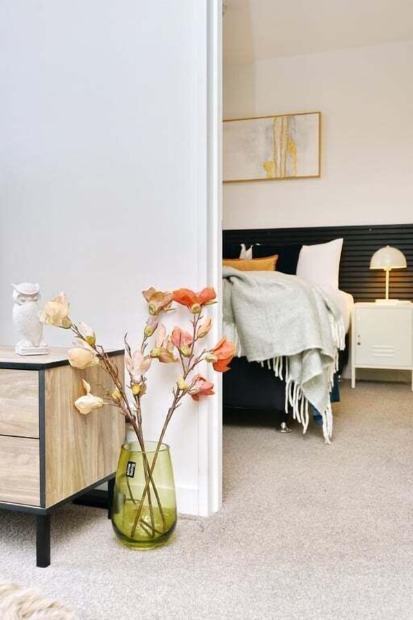Un dormitorio con cama, mesita de noche, lámpara y un jarrón con flores.