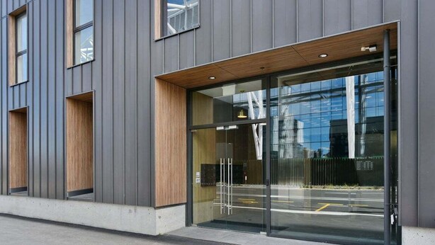 Un edificio moderno con amplios ventanales de vidrio y un alero de madera sobre la entrada.