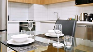 Una cocina moderna con baldosas blancas, un microondas negro y una mesa de comedor lista para dos personas, con platos y vasos blancos.