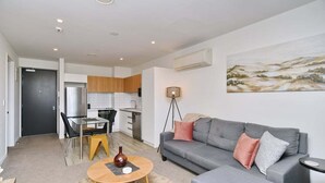 Un apartamento moderno con un sofá gris, una zona de comedor con una silla amarilla y una cocina al fondo.