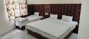 Ein Hotelzimmer mit zwei Einzelbetten und einem Doppelbett, alle mit weißer Bettwäsche.