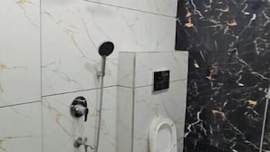 Een badkamer met witte en zwarte marmertegels, een douche, een toilet en een groene emmer.