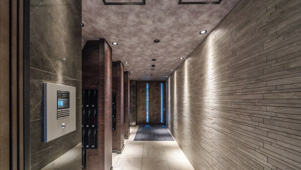 A modern hallway with a marble floor, a digital elevator control panel, and a brick-patterned wall.