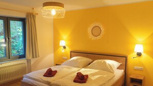 A double bed with two pillows, a bedside table, a lamp, and a window with curtains.