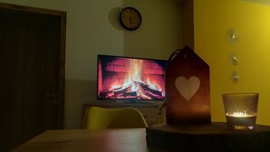 A room with a wooden table, a television displaying a fireplace, a heart-shaped decoration, and a candle holder.