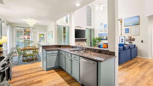 A modern kitchen with a granite countertop, built-in dishwasher, and a dining area with a table and chairs. - The Painted Paddle: Pool, HotTub, Pickleball Court (Lake Dallas)