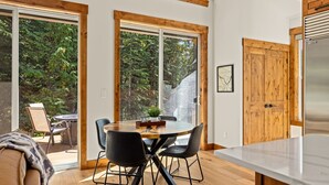 Une cuisine moderne dotée de grandes fenêtres, un coin repas avec une table ronde et des chaises, et une vue sur l’extérieur.