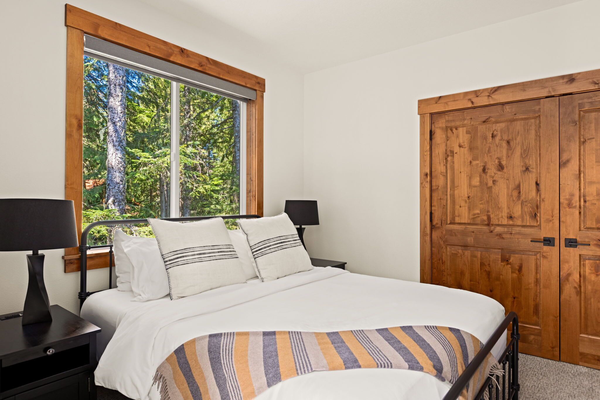 Quarto com uma janela grande, cama com roupa de cama branca, duas mesas de cabeceira com abajures e um guarda-roupa de madeira.