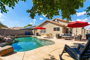 A backyard with a swimming pool, patio furniture, and a house.