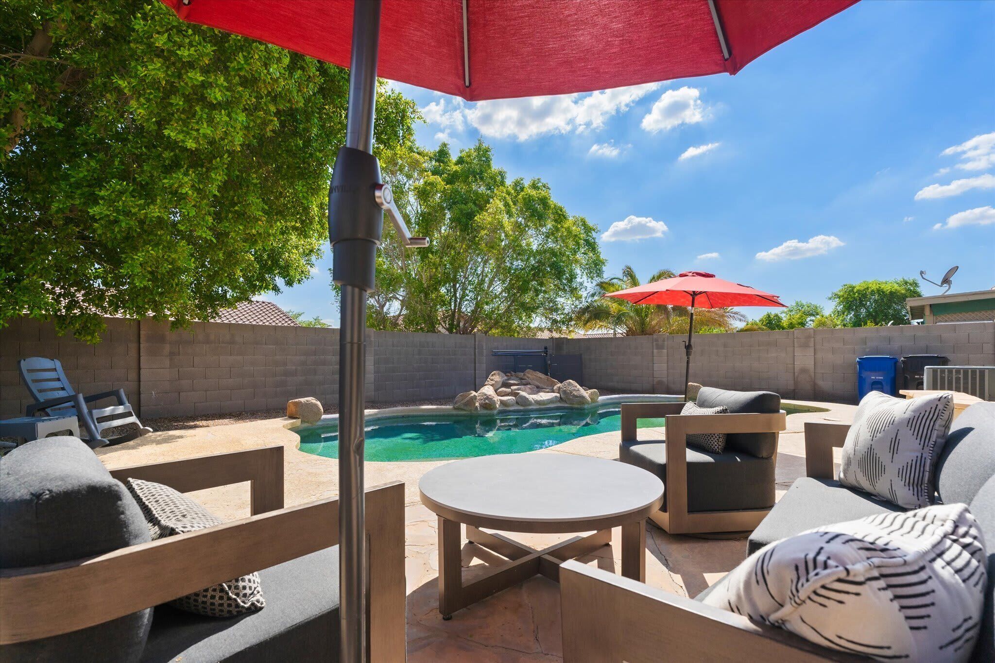 A backyard with a pool, patio furniture, and a red umbrella.