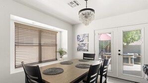 A dining area with a wooden table, black chairs, and a chandelier. - The Sun Club | Private Pool • BBQ • Outdoor Dining (Mesa)