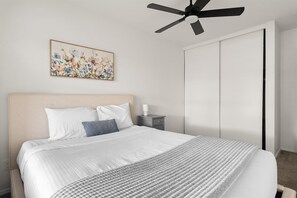 A bedroom with a bed, a ceiling fan, a nightstand, a bedside table, and a wardrobe.