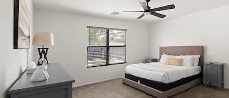 A bedroom with a bed, bedside tables, a ceiling fan, a window, and a desk with a lamp.