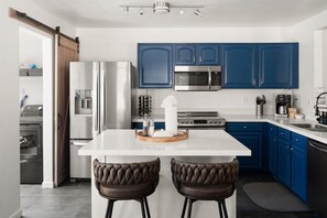 Una cucina moderna con mobili blu, elettrodomestici in acciaio inossidabile, un'isola centrale con sgabelli e una porta a soffietto in stile rustico.