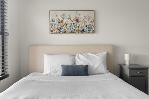 A hotel room with a bed, a nightstand, a lamp, and a painting on the wall. - The Sun Club | Private Pool • BBQ • Outdoor Dining (Mesa)