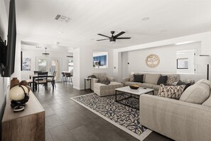 A modern living room with a sofa, coffee table, and a dining area with chairs and a table.