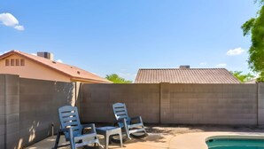 A backyard with a swimming pool, two lounge chairs, and a brick wall. - The Sun Club | Private Pool • BBQ • Outdoor Dining (Mesa)