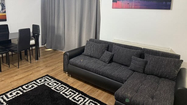 Una sala de estar moderna con un sofá gris, una mesa de comedor con sillas, un tapete negro y un cuadro de un paisaje urbano.