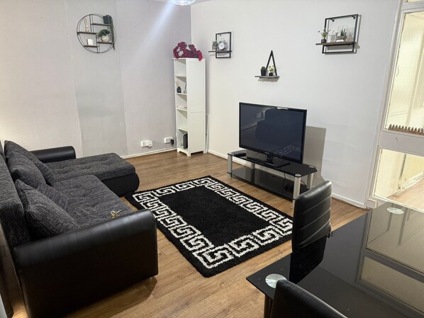 Ein Wohnzimmer mit einer Couch, einem Fernseher, einem Couchtisch und einem dekorativen Teppich.