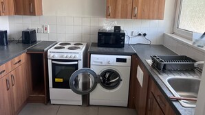 Cocina compacta con armarios de madera, estufa, microondas, lavadora y fregadero.