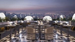 Uma área externa com mesas e cadeiras, vista para a cidade e piso de azulejos.
