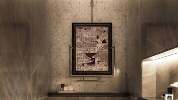 A modern bathroom with a hexagonal patterned wall, a framed artwork, a toilet, and a shower.