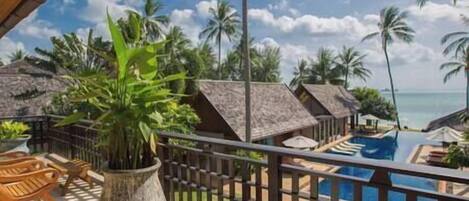 A resort with thatched-roof bungalows, a pool, and a view of the ocean.