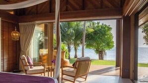 Een kamer met een bed, twee stoelen, een tafel en uitzicht op zee en palmbomen.