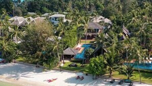 Een resort met een zwembad, strand en palmbomen.