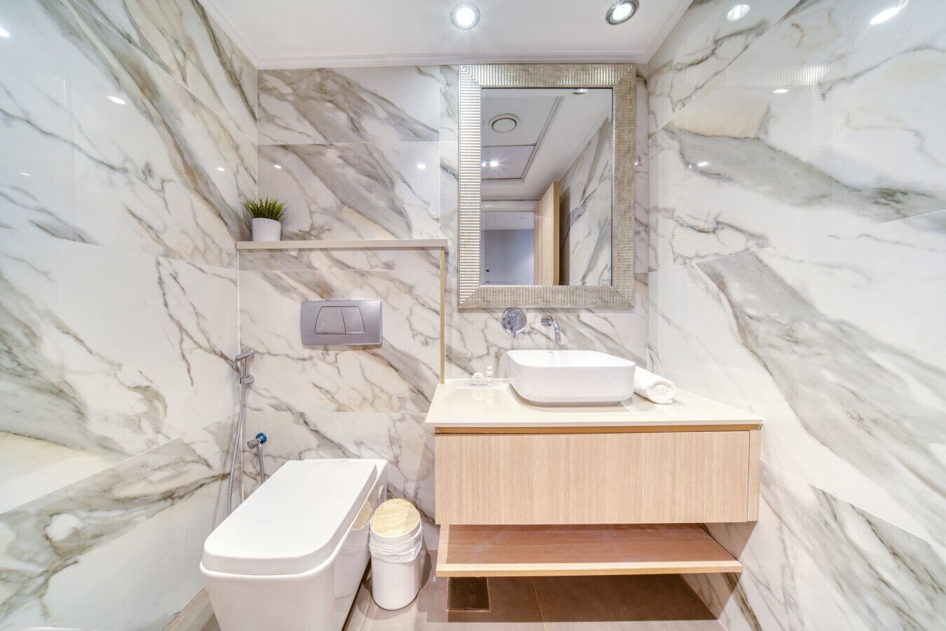 Ein modernes Badezimmer mit Marmorwand, Waschtisch aus Holz, weißem Waschbecken, Dusche und Toilette.