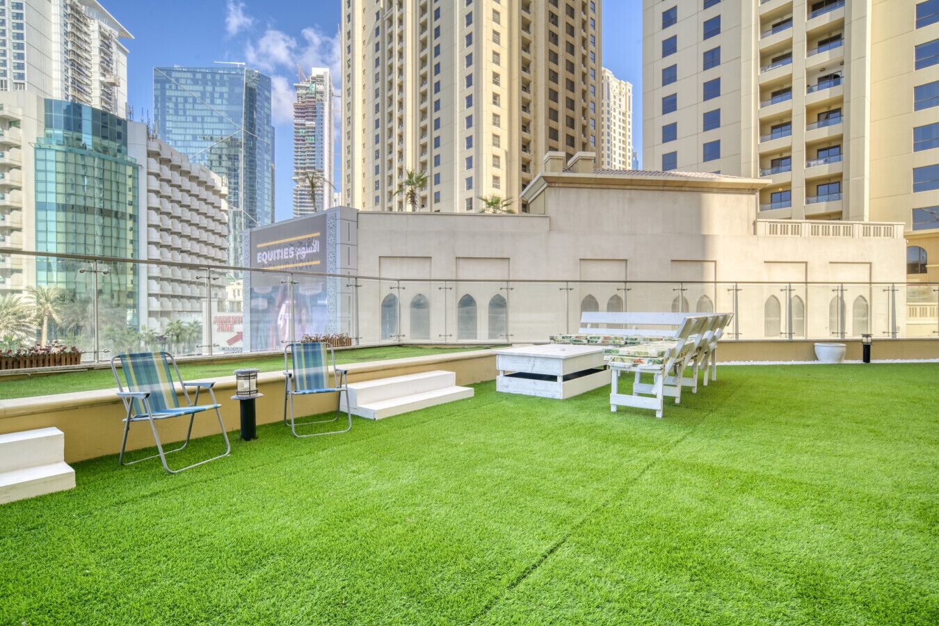 Un jardín en la azotea con césped artificial, mobiliario exterior y vistas de edificios altos circundantes.