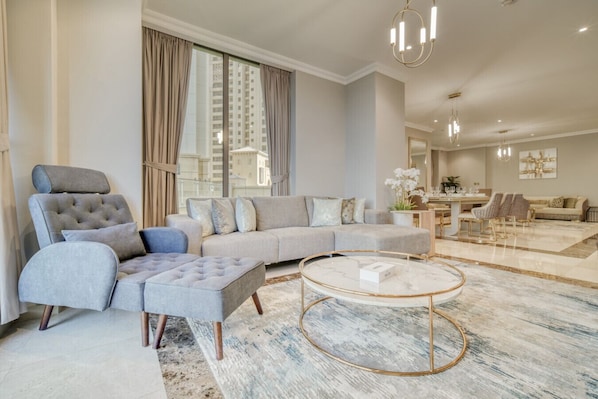 A modern living room with a grey sectional sofa, a tufted armchair, and a round coffee table with a gold frame.