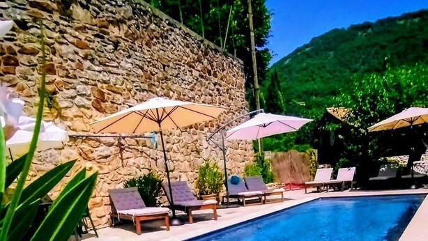 A swimming pool with lounge chairs and umbrellas, surrounded by stone walls and greenery. - Mes Maisons Charming 3-bedroom Gite with AC, fitness room in delightful Cevennes (Gagnières)