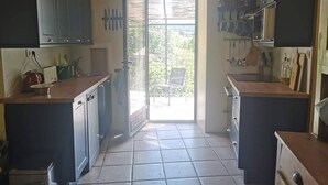 A kitchen with a central island, cabinets, and a view through a glass door to an outdoor area. - Mes Maisons Charming 3-bedroom Gite with AC, fitness room in delightful Cevennes (Gagnières)