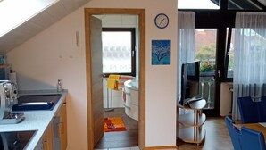 A modern kitchen with a built-in oven, a dining area with a blue chair, and a view through a doorway to a living room. - Holiday Apartment 60sqm, 2 Bedrooms, Max. 4 Persons, 4 Stars - DTV Classified (Hayingen)