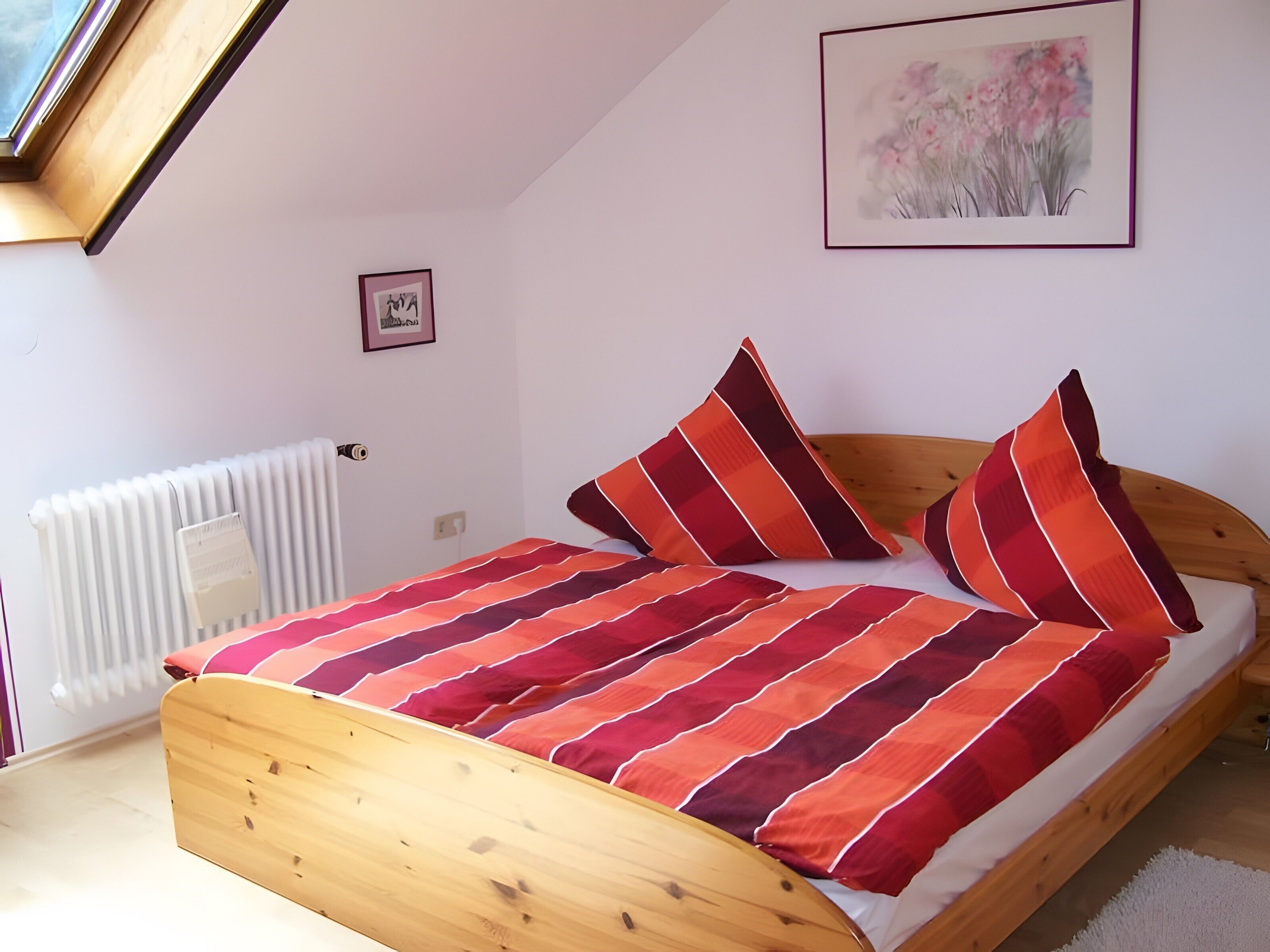 Un dormitorio con una cama de madera, un radiador, un cuadro enmarcado y un tragaluz.
